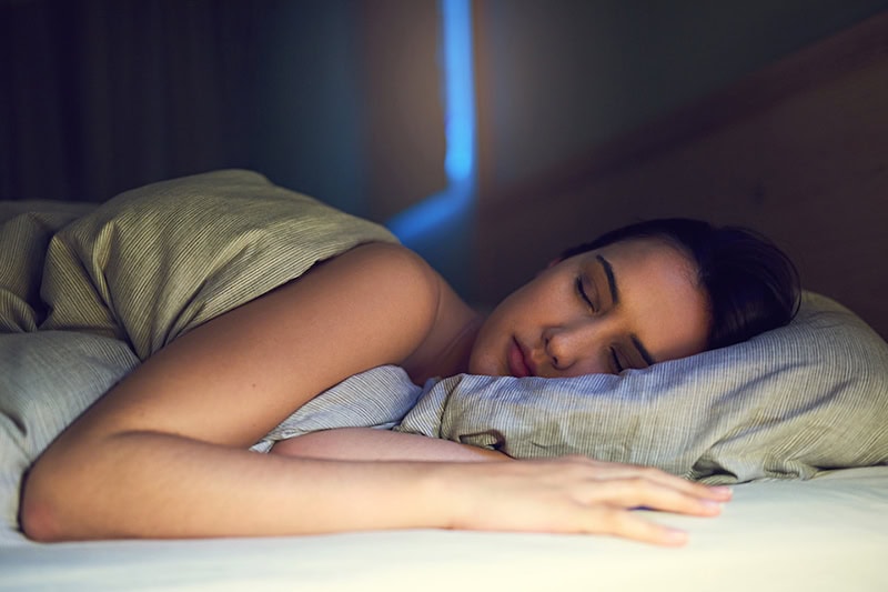 3 Health Benefits for Using Your AC While Sleeping. Young woman sleeping soundly in her bed.