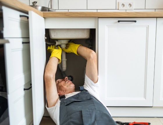A Raymond Plumbing Heating & Air Conditioning plumber repairing a sink.